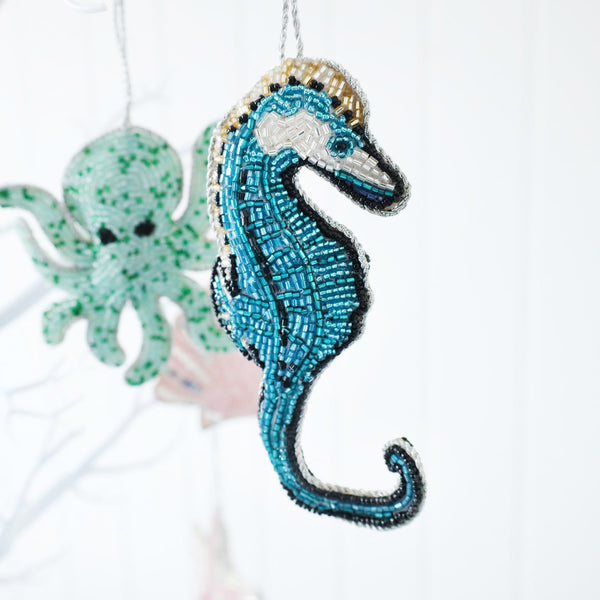 beaded blue and turquoise christmas decoration in the shape of a seahorse hanging on a tree,aqua octopus in the background