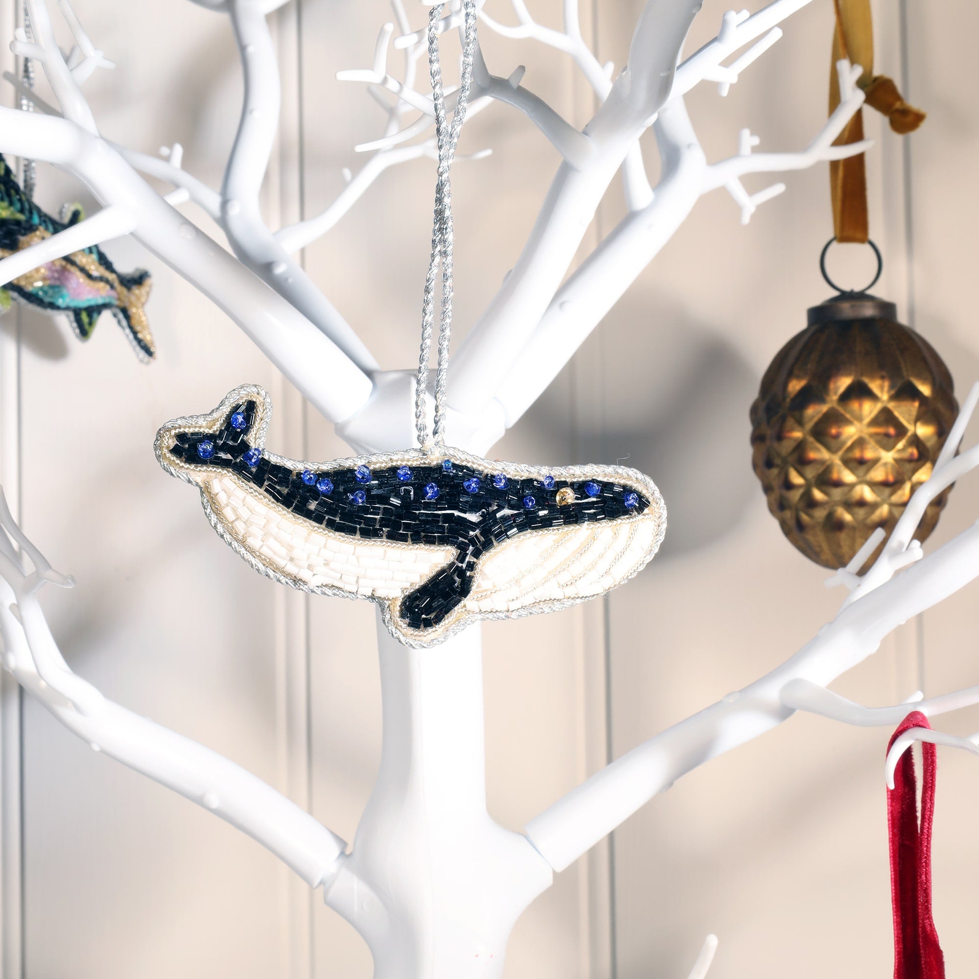 beaded whale christmas decoration hanging on white branched chritmas tree.