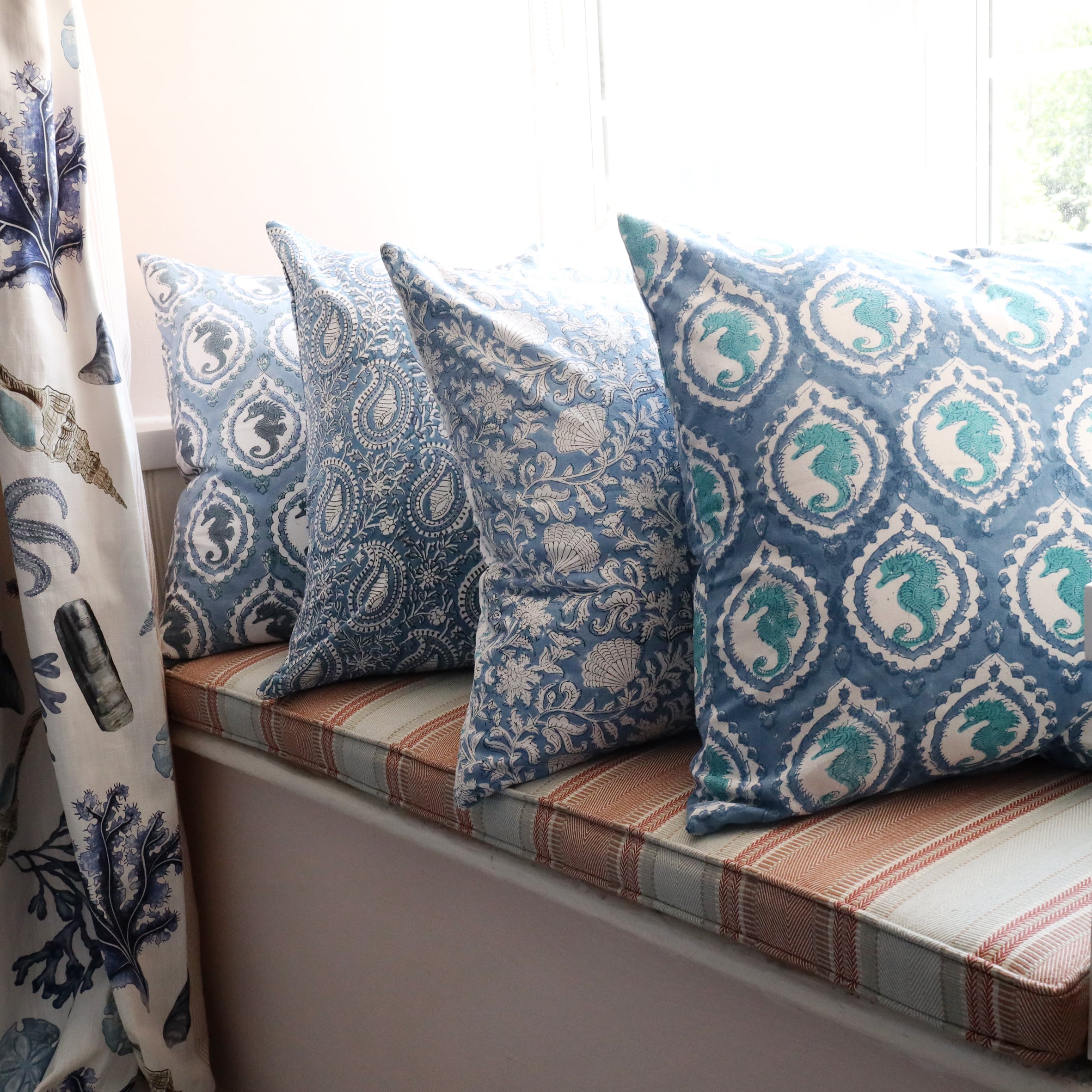 Ocean Blue Seahorse Cameo cushion which is Hand block printed fabric on a window seat.Also on the seat are other Hand block printed cushions,you can see the Rockpool Curtains to the side.