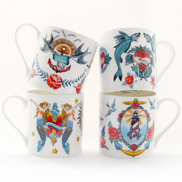 Set of 4 white bone china mugs decorated in brightly coloured sailor's tattoo inspired designs all against a white background. There are swallows ansd anchors, sharks and hearts, mermaids and daggers and lighthouse and kraken.