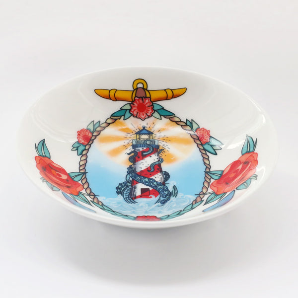 product shot of a white bone china nibbles dish decorated with a red and white lighthouse with a krakens tentacles coming through the windows. This is surrounded by a rope, roses and anchor. All of this is illustrated in a tattoo style.
