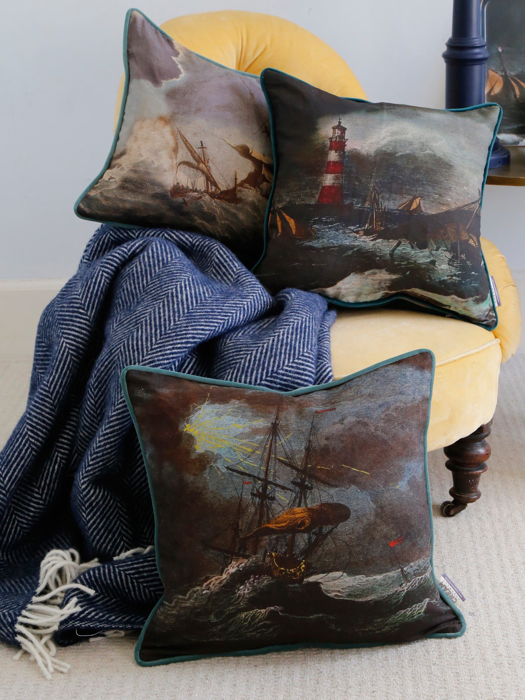 Shipwreck Night Cushion Square Cover placed on a chair with other shipwreck cushions.All piled  with a navy throw all placed on a mustard velvet chair