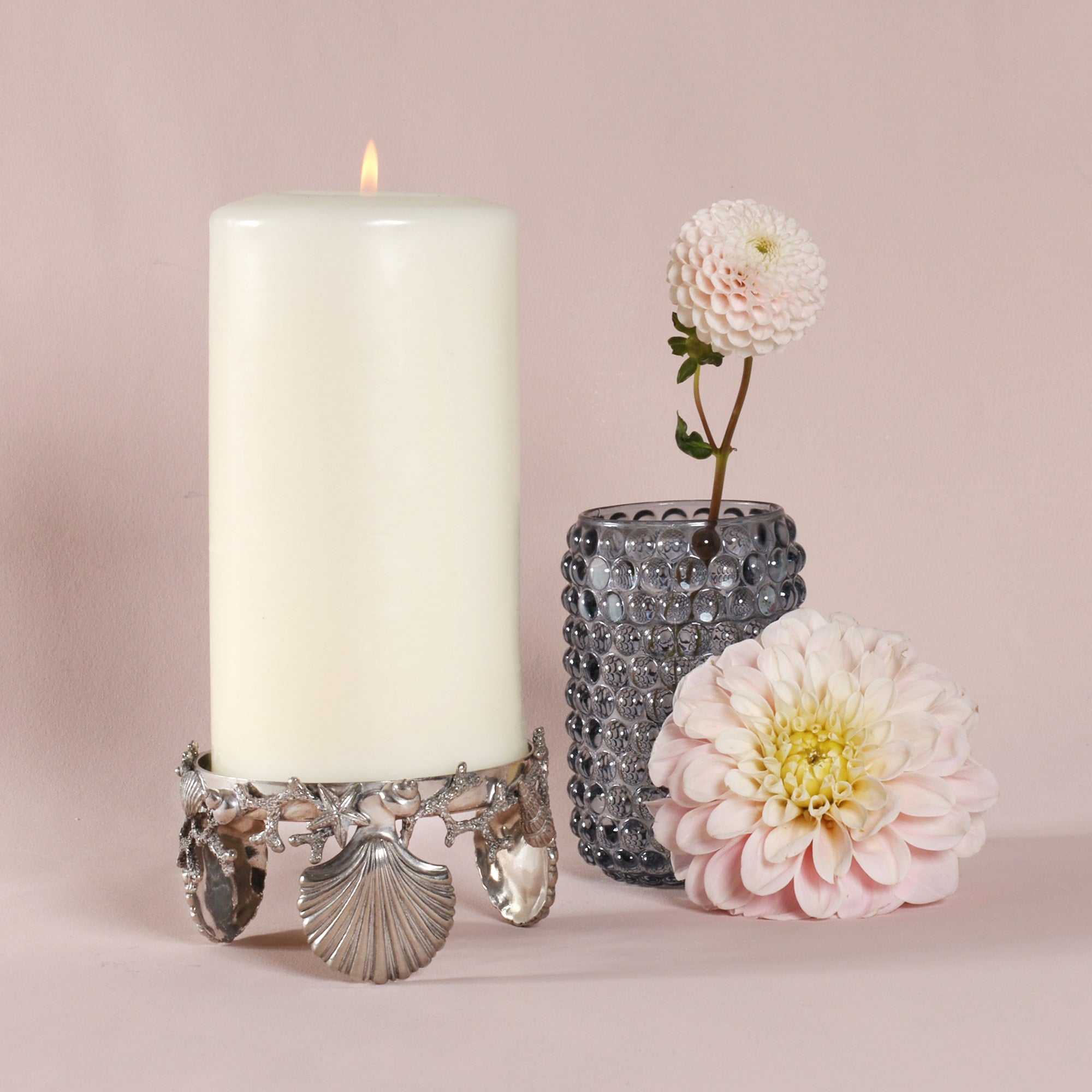 Shell and Coral Candle Holder holding a large candle.Next to the item is a glass containing flowers