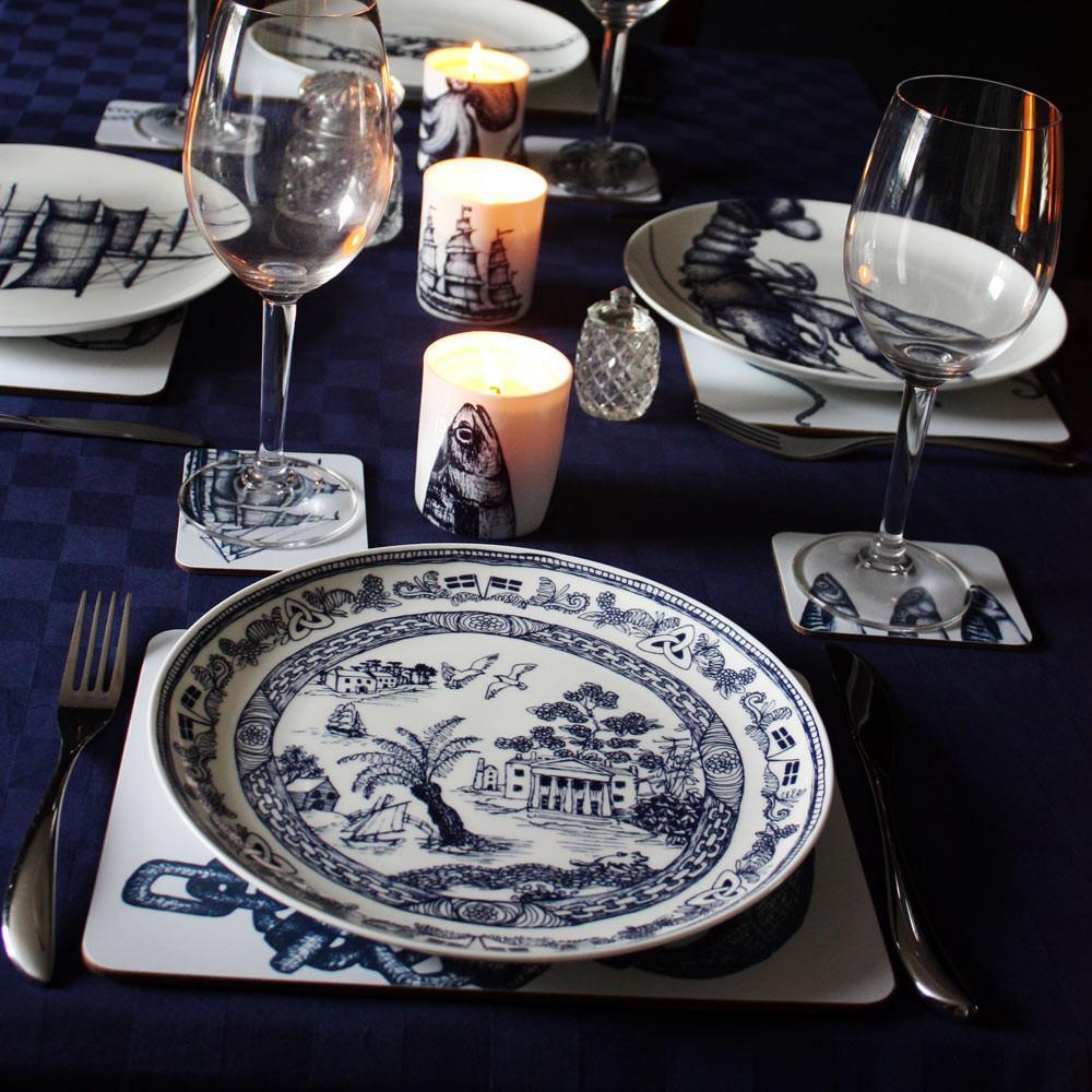 Bone China White 26cm diameter plate with beautifully hand drawn illustrations our classic Willow design with typically Cornish scenes in Navy.It is on a four place setting with other designs and matching placemats,coasters and a couple of our Bone china candles are setting the scene