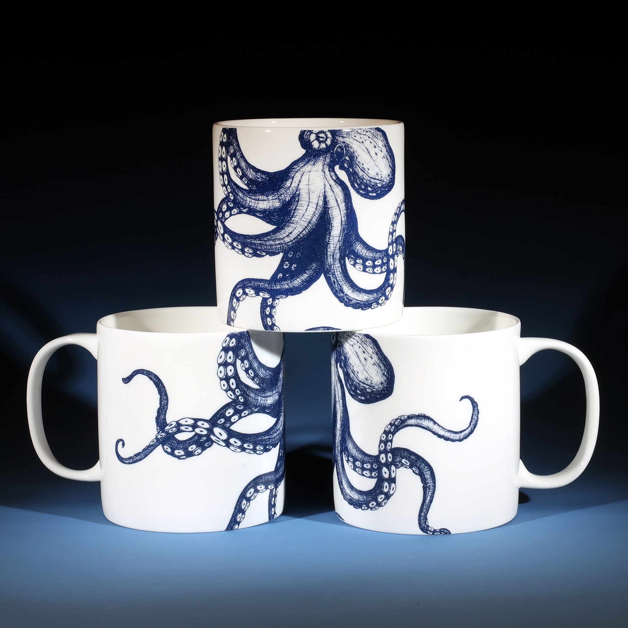 3 white bone china mugs with a navy blue octopus illustration on. The 2 at the bottom have the handles facing outwards and the one on the top is facing forward, so that you can see the mug from every angle.