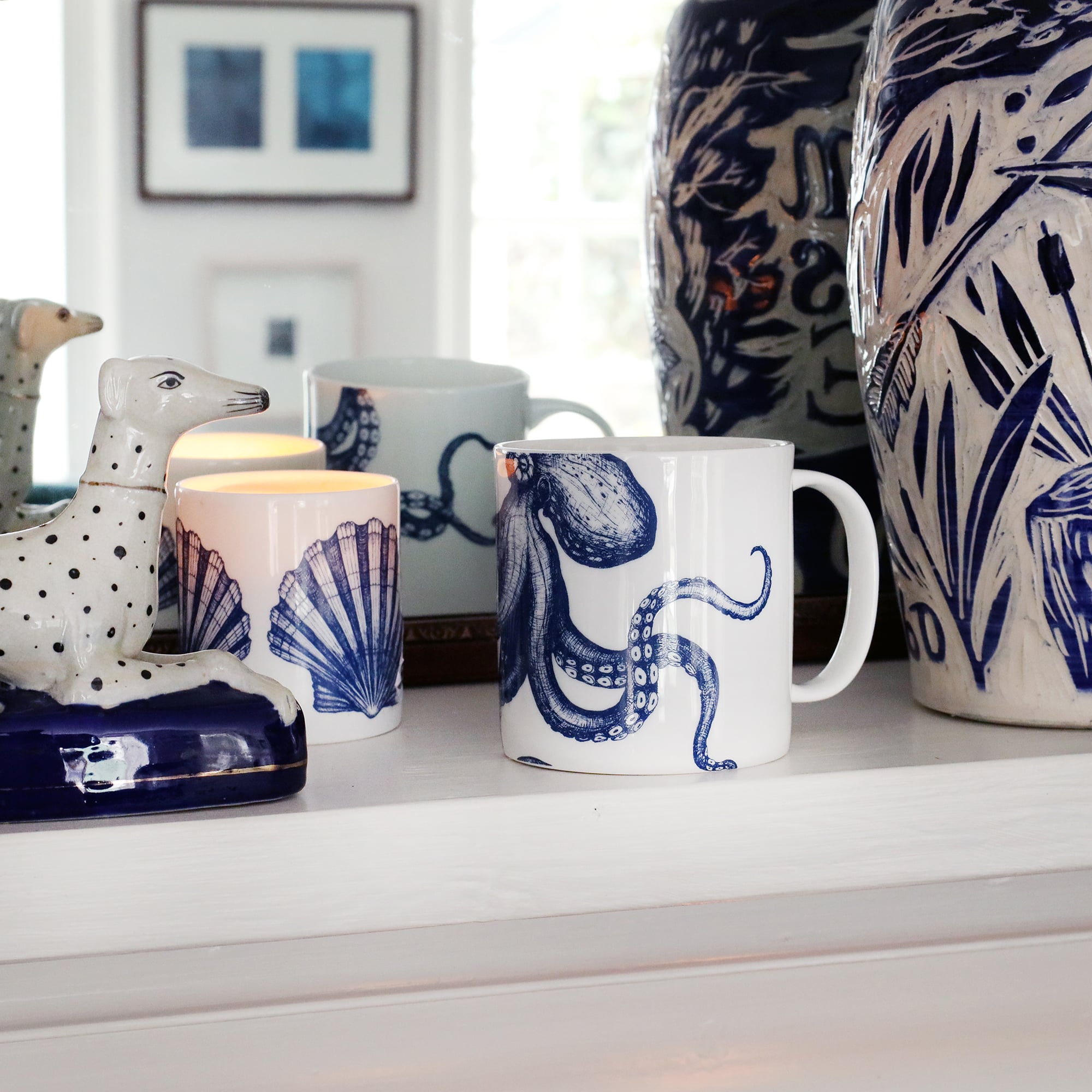 White bone china mug with a navy illustrated octopus on, sitting on a mantlepiece with other blue and white items and reflected in a mirror behind.