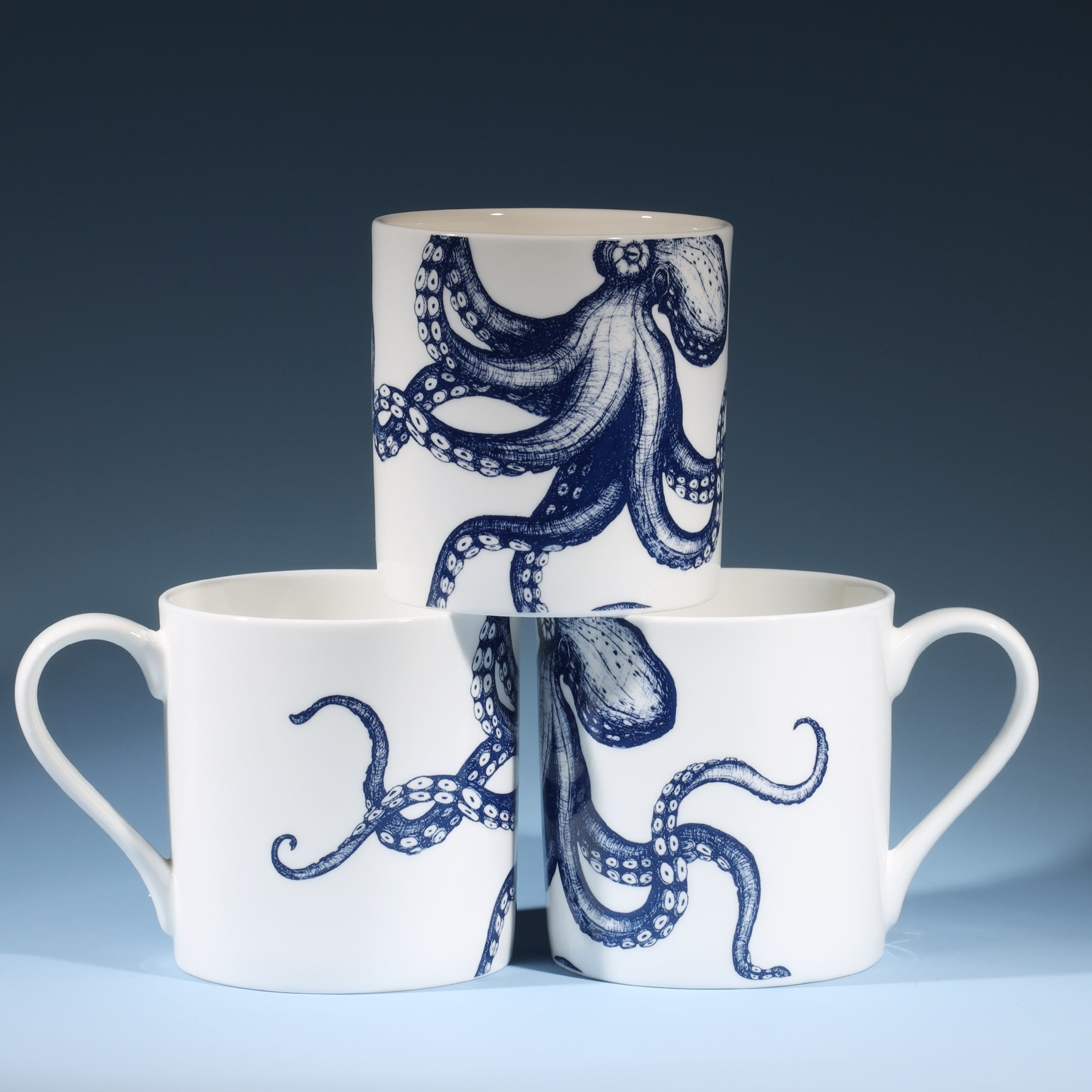 The photo shows a Bone china  mug featuring a hand drawn octopus design in classic  blue and white in a stack of three showing all sides