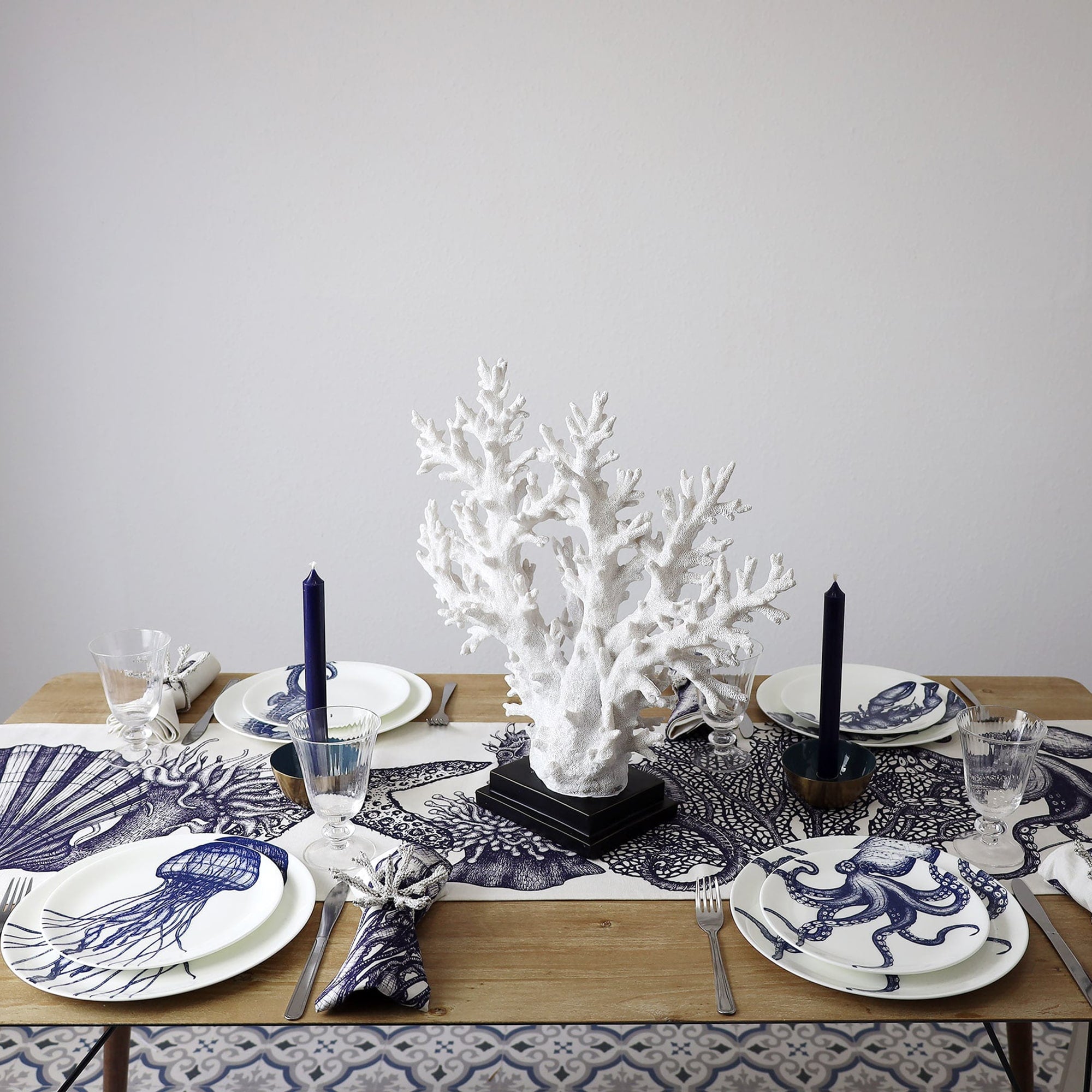 Cotton and Linen mix table runner with hand drawn illustrations of Navy Octopus,Crab,Seahorse and others from our classic sea creatures in Navy on white placed on a table.Also on the table ia a centrepiece of white coral and the table is laid up with our classic china and other tableware
