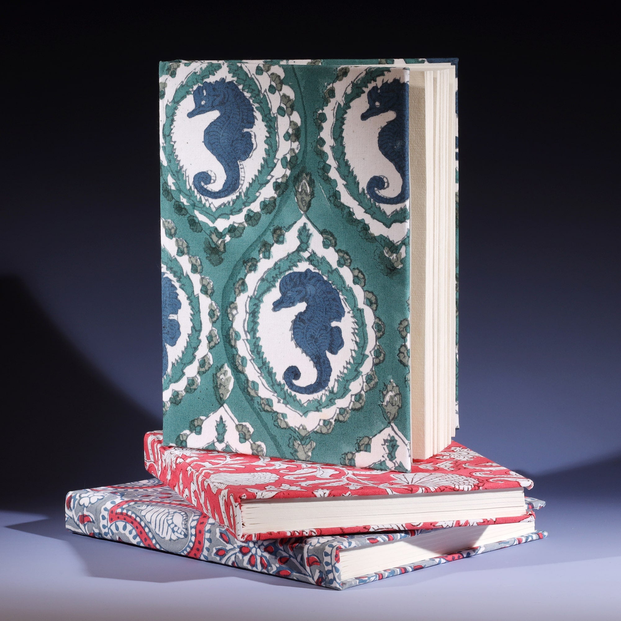 Hand Block printed hard backed notebook Seahorse Cameo in Ocean on its side placed on a stack of other notebooks