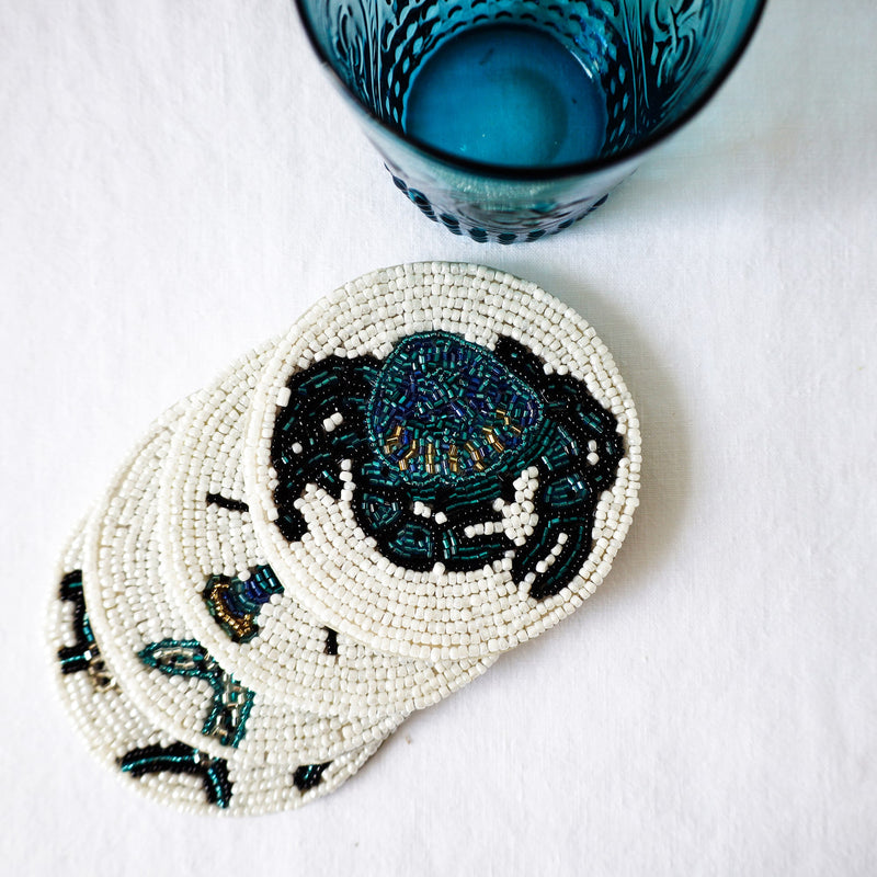 Handmade glass beaded coaster with a Crab design on a stack of other glass coasters next to a glass 