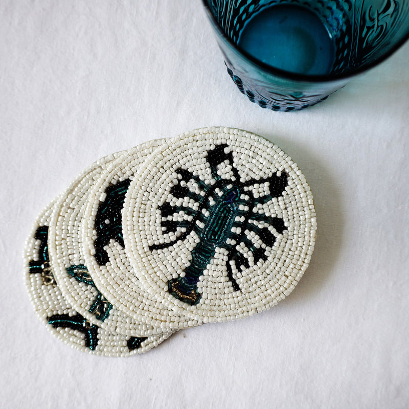 Handmade glass beaded coaster with a Lobster design on a stack of other glass coasters next to a glass