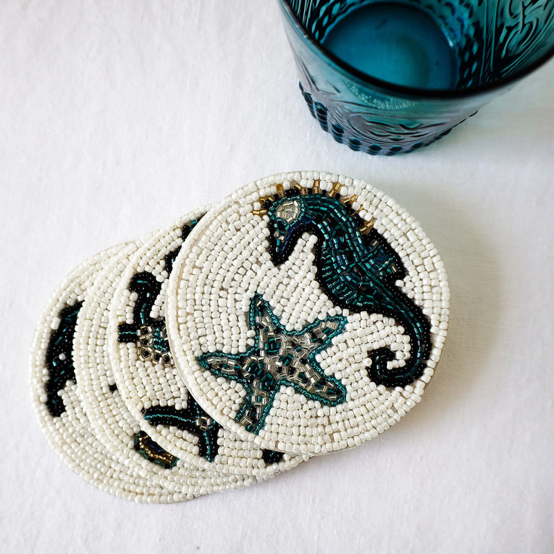 Handmade glass beaded coaster with a Seahorse and Starfish design on a stack of other glass coasters next to a glass