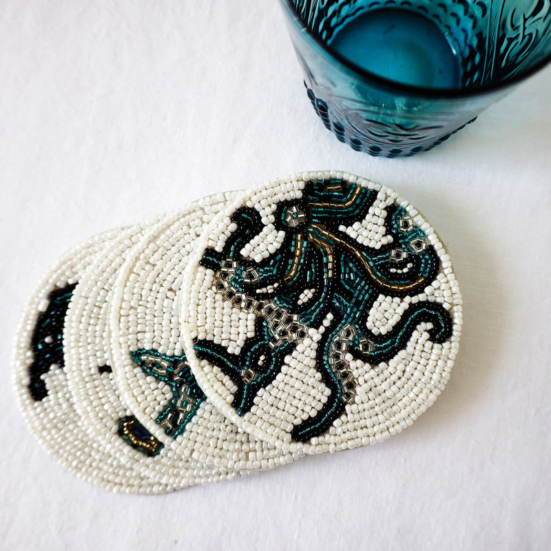 Handmade glass beaded coaster with a Octopus design on a stack of other glass coasters next to a glass