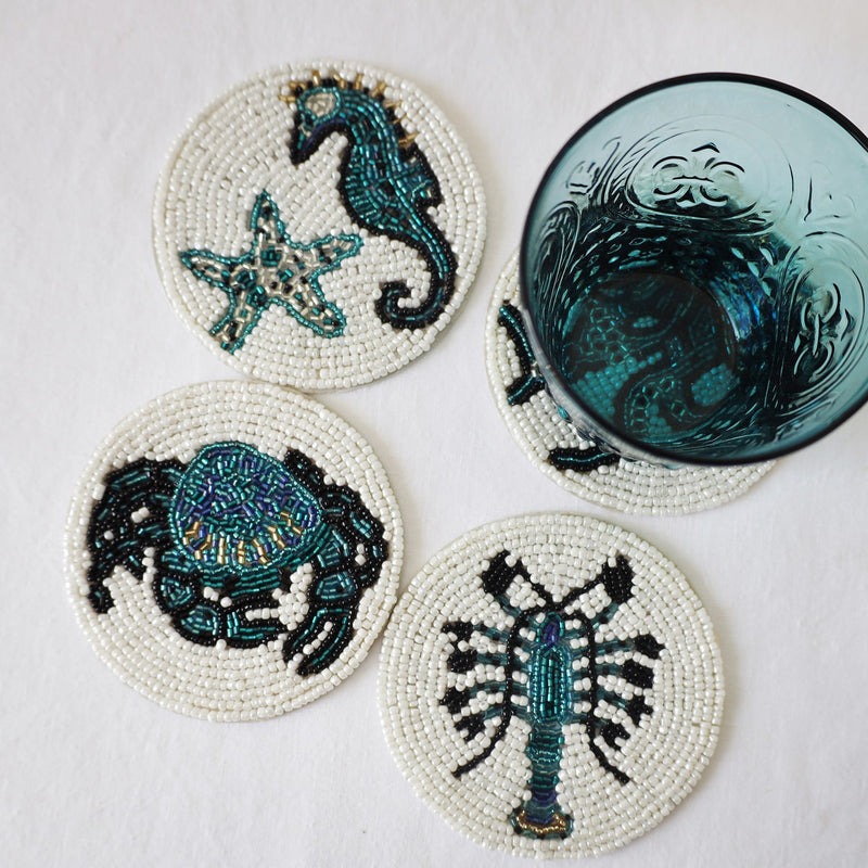 Handmade glass beaded coasters in Starfish and Shell,Octopus,Crab and Lobster,the Octopus is obscured by a glass.