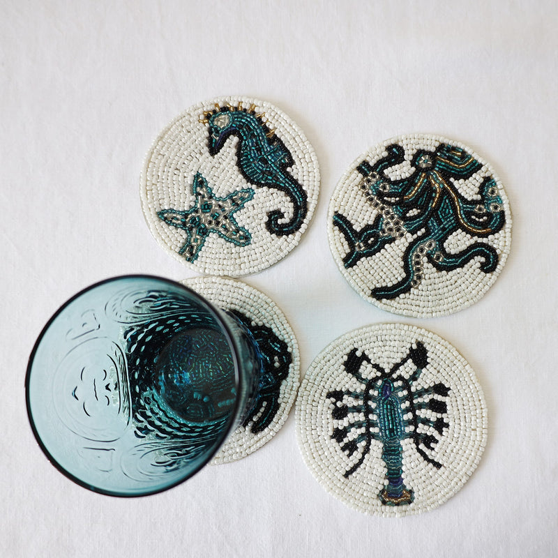 Handmade glass beaded coasters in Starfish and Shell,Octopus,Crab and Lobster,the Crab is obscured by a glass.