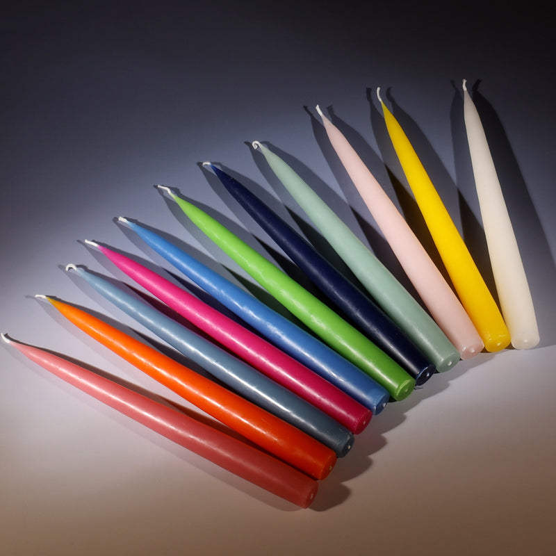 fan of 11 different coloured dinner taper candles lying on a graduated pink to blue ombre background