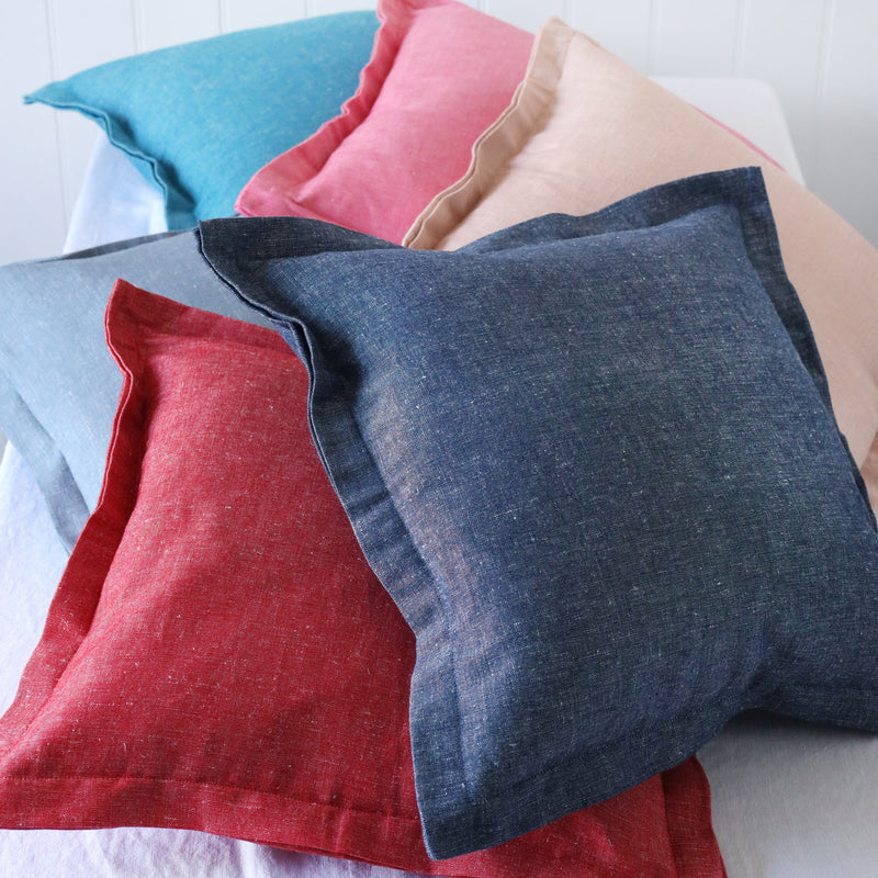 6 chambray cushions in blues, red and pinks in a pile and shot from above