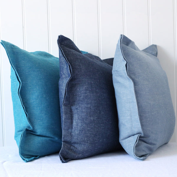 turquoise, navy and light blue chambray cushions with double flange in a row on white background