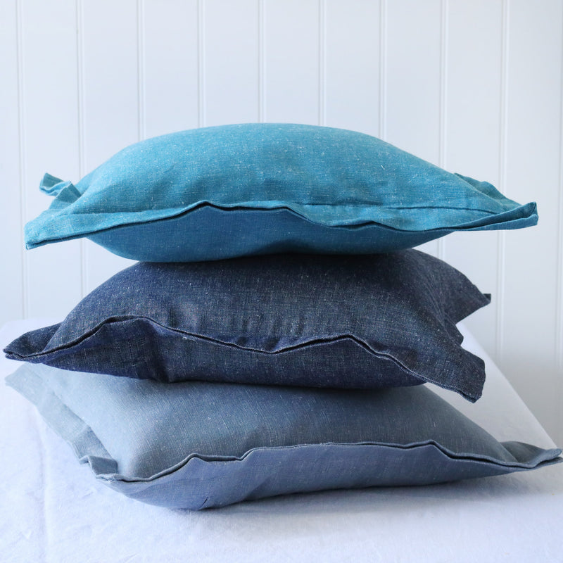 turquoise, navy and light blue chambray cushions with double flange in a pile on white background