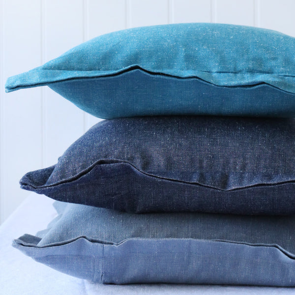 detail of turquoise, navy and light blue chambray cushions with double flange in a pile on white background