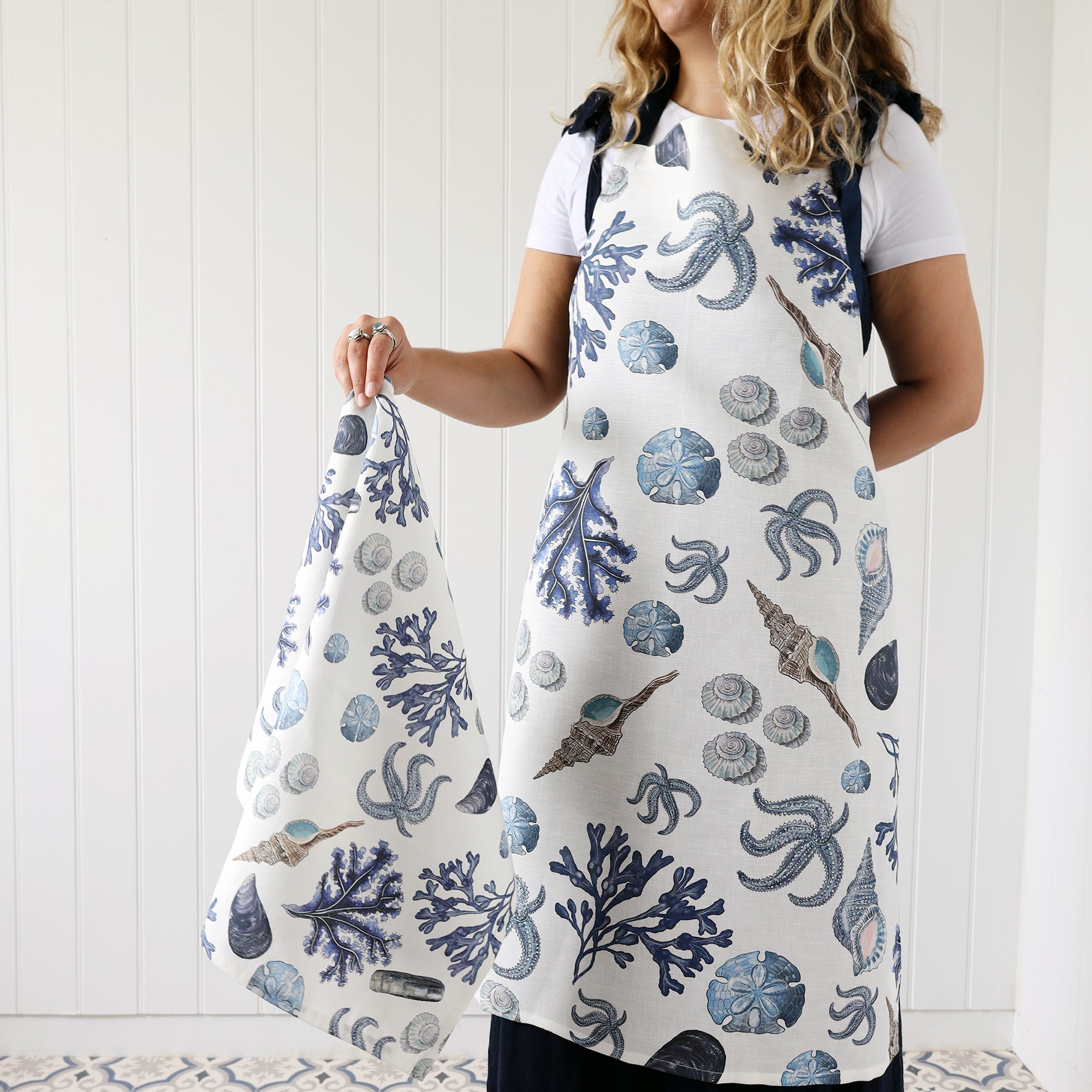 Our beachcomber apron being worn by a model who is also holding a beachcomber tea towel