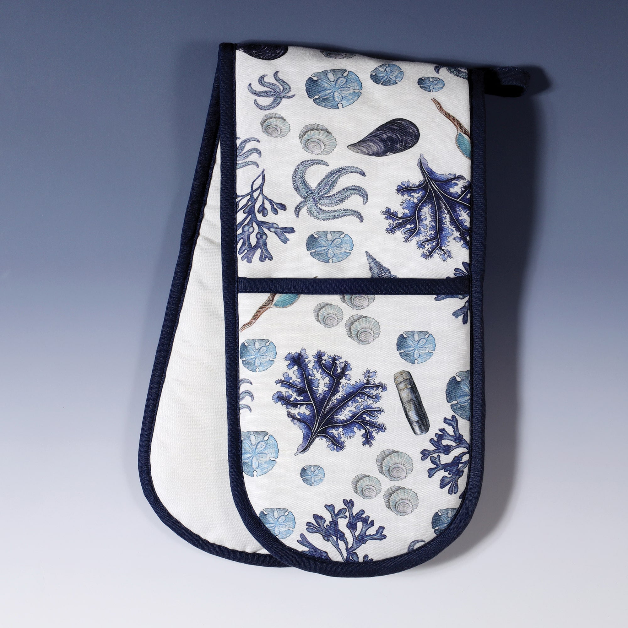 Oven gloves with all over design of sea shells and seaweed in blues on white background with a navy trim in our beachcomber design