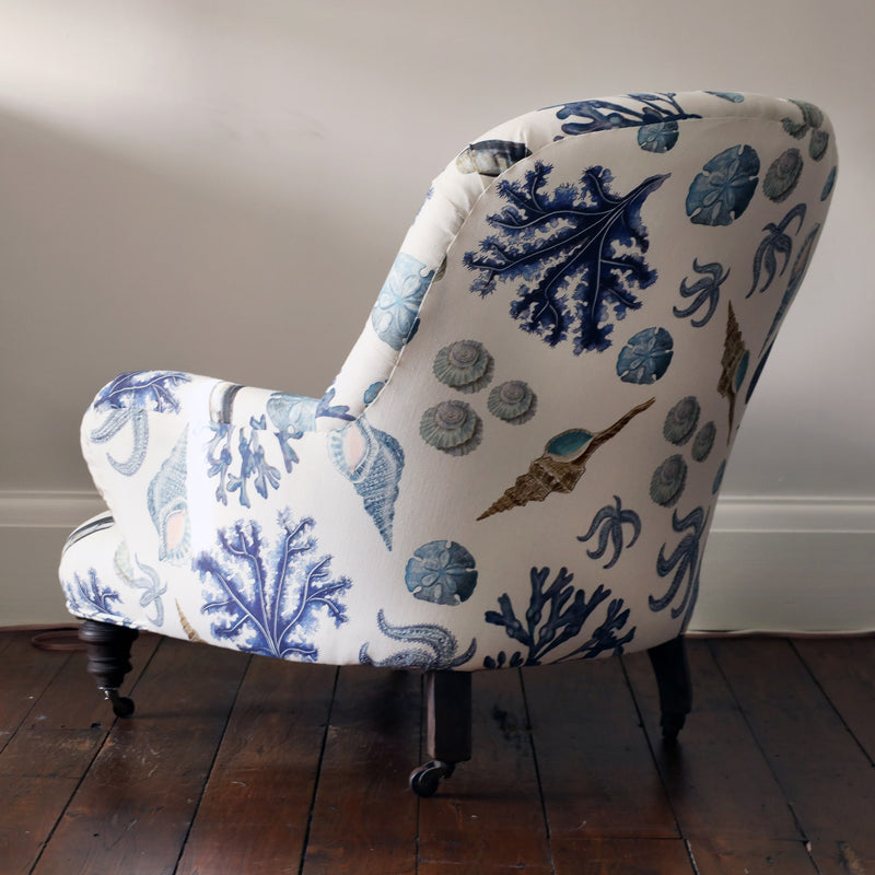 Back & side view of a re upholstered victorian button back armchair covered in a shell and seaweed fabric in blue tones on an off white background.