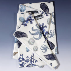 Cotton and Linen mix table runner with hand drawn illustrations with our Rockpool design of Sea life and Shells in shades of Blue folded to show different shells