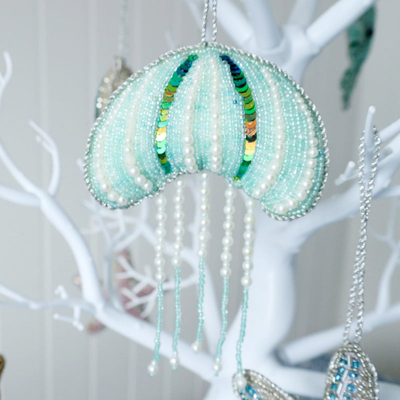 beaded aqua christmas decoration in the shape of a jellyfish with 5 strands of dangling pearl and glass bead tentacles hanging from a tree