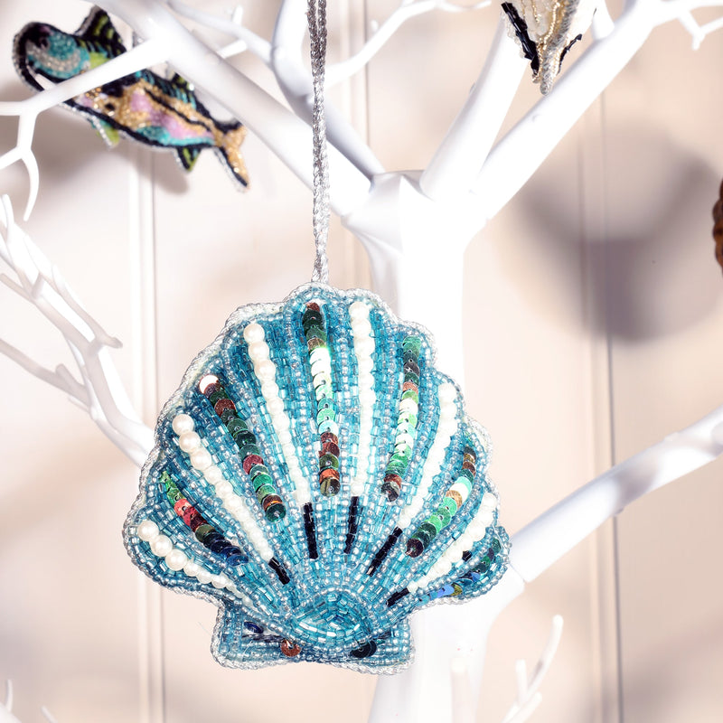 beaded and sequined blue scallop shell christmas decoration hanging on white branched christmas tree.
