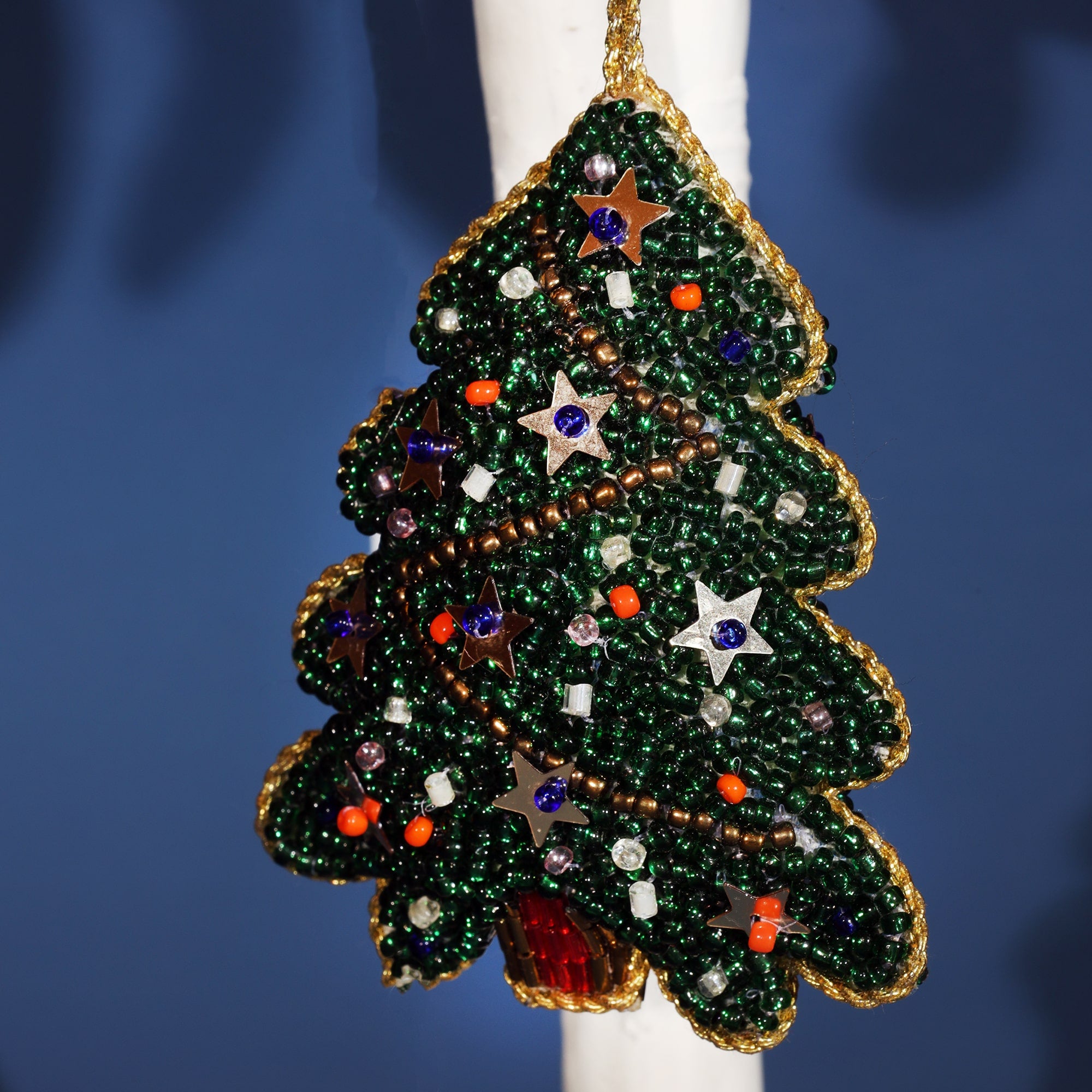 A beaded Christmas tree ornament adorned with green beads, gold trim, and colorful decorations. The tree is decorated with small beads in various colours, including orange, white, and purple, along with silver star-shaped sequins. The ornament is outlined in gold beads, giving it a festive sparkle.