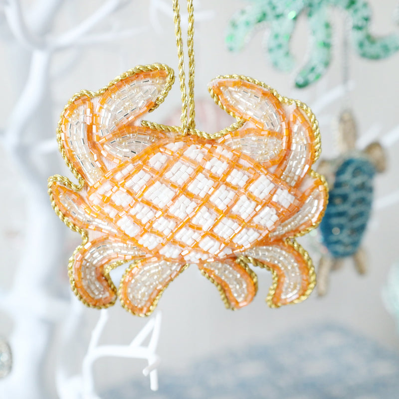 beaded orange and gold christmas decoration in the shape of a crab hanging from a tree,you can see the turtle decoration hanging in the background