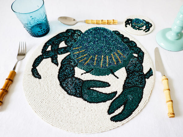 Handmade glass beaded placemat with a Crab design in Navy,Black and gold on white glass beads in a place setting with cutlery,a glass and a candlestick