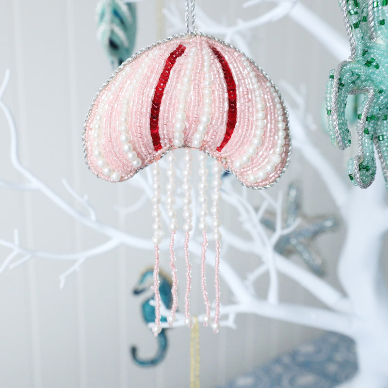 beaded pink christmas decoration with red sequins and white pearls hanging from a tree