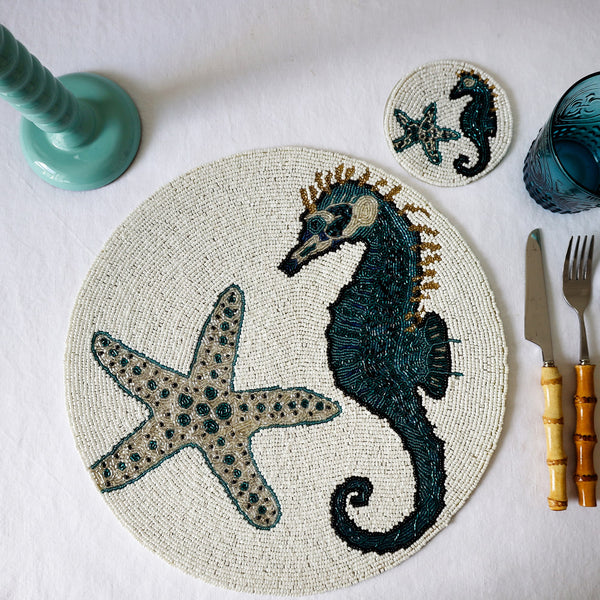 Handmade glass beaded placemat with a Seahorse and Starfish design in Navy,Black and gold on white glass beads in a place setting with cutlery,a glass and a candlestick