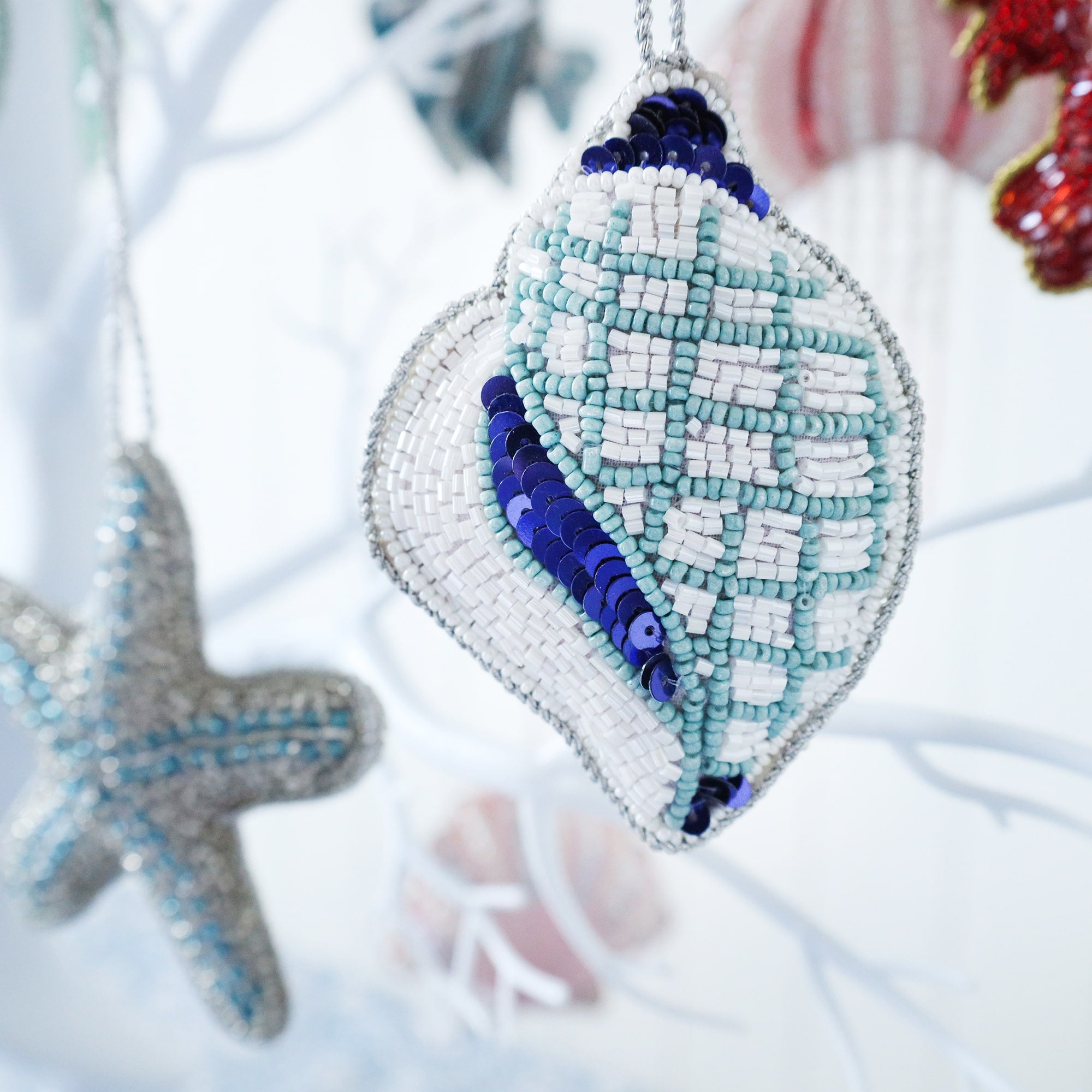 beaded blue and white christmas decoration in the shape of a conch shell hanging on a tree with a blue starfish in the background