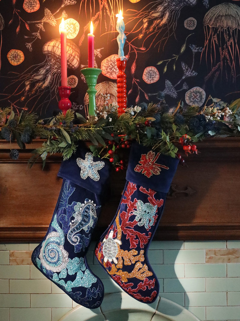 2 dark blue velvet beaded christmas stocking decorated with sea creatures and corals hanging from a mantlepiece with foliage and berries. 