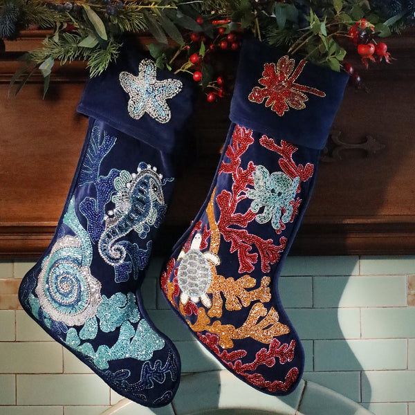 2 dark blue velvet beaded christmas stocking decorated with sea creatures and corals hanging from a mantlepiece with foliage and berries. 