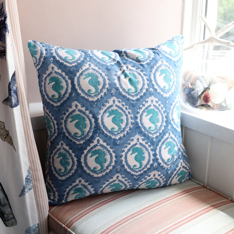 Marine Blue Seahorse cushion which is Hand block printed fabric in a soft blue and turquoise seahorse in a cameo design on a window seat.On the window ledge is a jar of shells on the window ledge