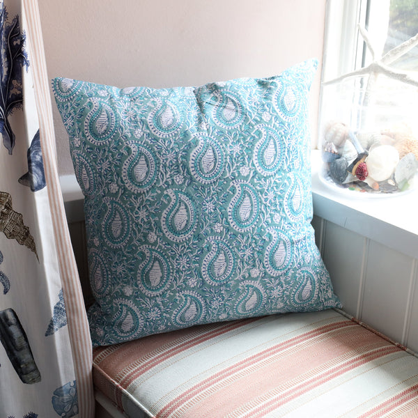 Sea Foam Paisley Shell cushion which is Hand block printed fabric in a soft blue and white on a window seat.You can see the Rockpool curtain in the foreground and a glass jar with shells in