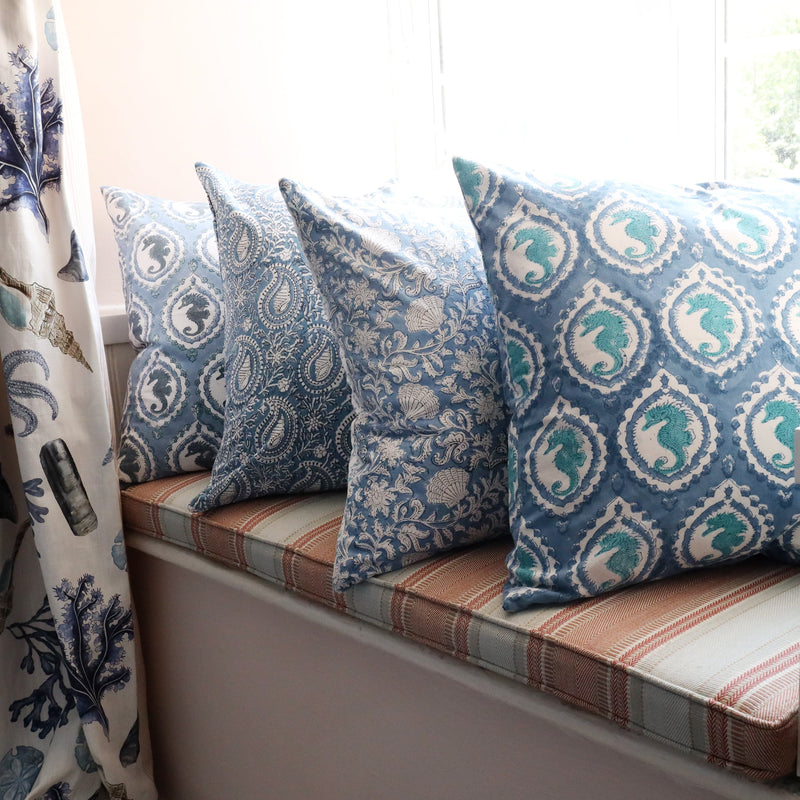 Azure Paisley Shell  cushion which is Hand block printed fabric  on a window seat.Also on the seat are other Hand block printed cushions,you can see the Rockpool Curtains to the side