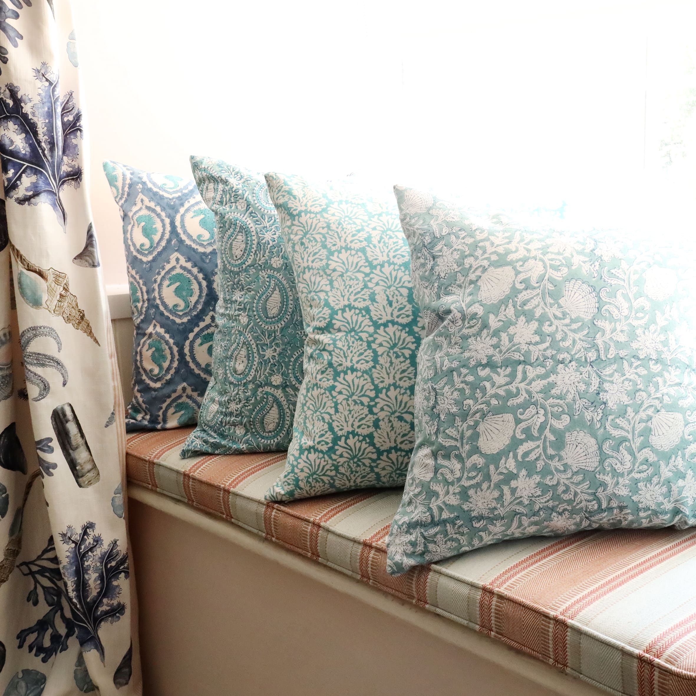 Sea Breeze Seashell Flower cushion which is Hand block printed fabric on a window seat.Also on the seat are other Hand block printed cushions,you can see the Rockpool Curtains to the side.