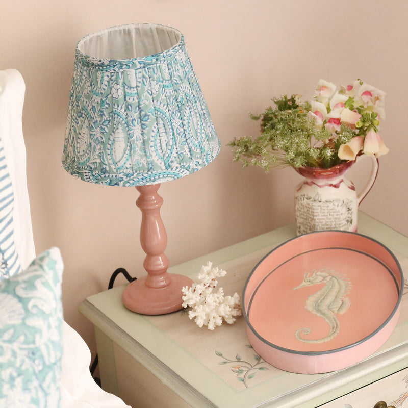 Small pleated Seafoam Paisley Shell lampshade in hand blocked print on a pink lampbase.The lampbase is on a bedside cabinet with a small jug with flowers and one of our hand painted seahorse  trays