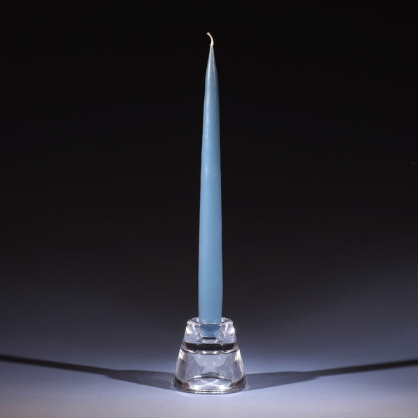 blue grey tapered dinner candle in a small glass candle holder on an ombre blue background