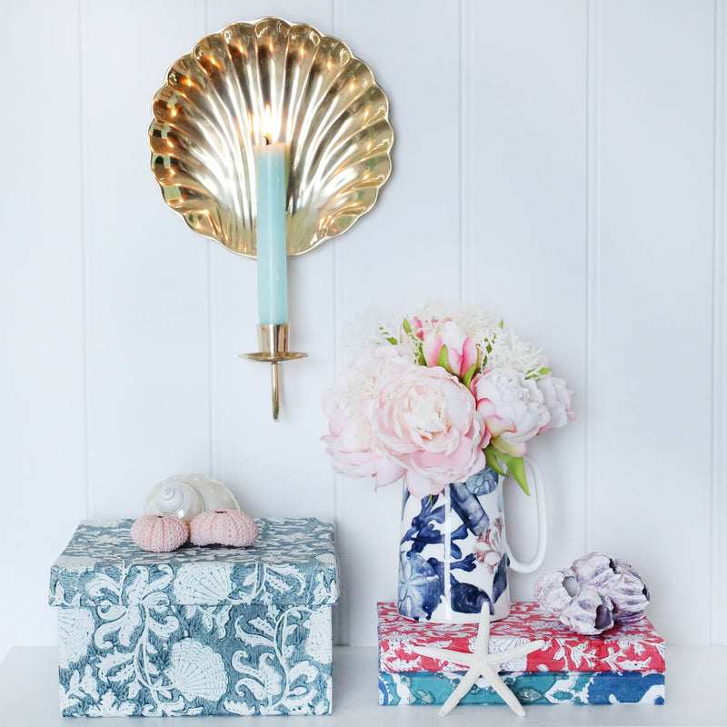 Medium Seashell Flower in Seabreeze hand blocked paper covered box on a shelf.On the shelf are a couple of notebooks and a beachcomber jug with flowers.On the box are some shells  and behind on the wall is a scallop Candle Sconce