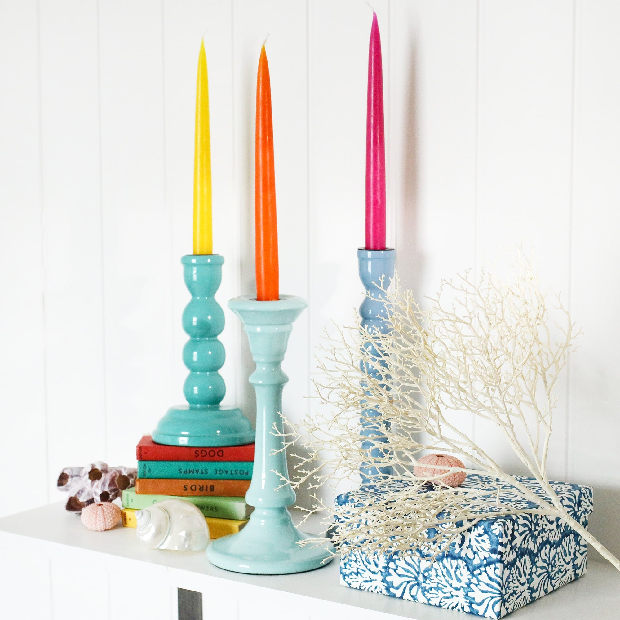 Turquoise candle holder placed on a couple of small coloured books.Next to this are a couple of candle holders and other decorative pieces on a shelf