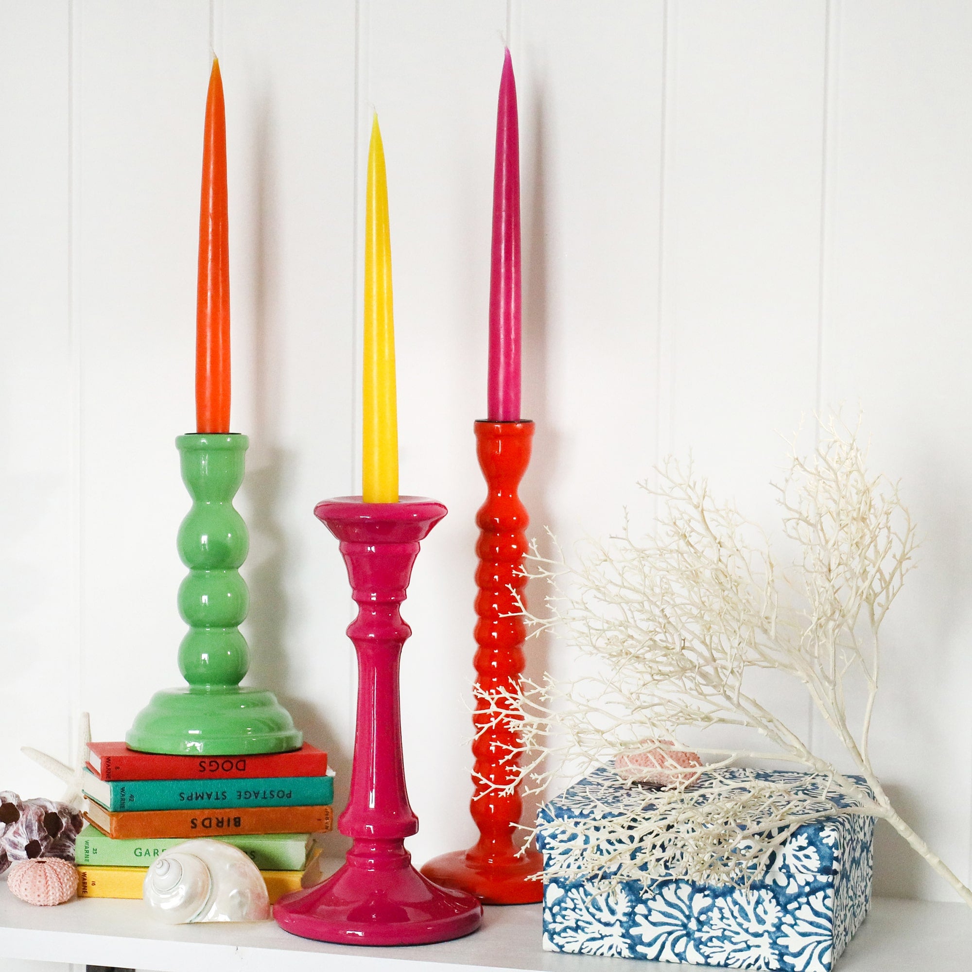 Candle holder placed on a couple of notebooks.Next to this is Fuschia Tidal candle holders.Both have contrasting candles in them,there are shells also in the picture