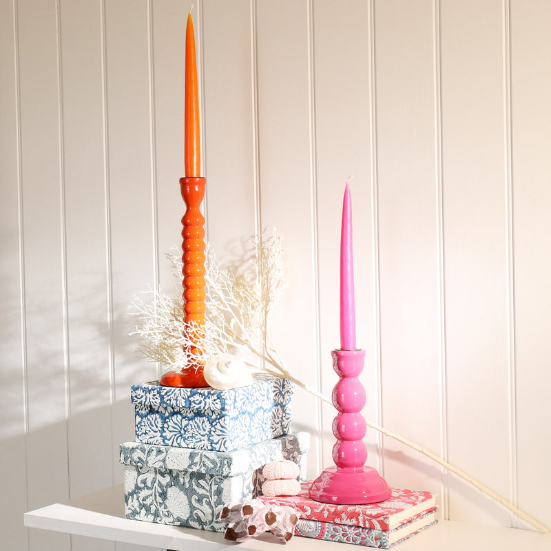 Sunset candle holder placed on a couple of hand painted boxes on a shelf.Next to this is another candle holder placed on a couple of hand blocked painted notebooks and other decorative pieces.Both candle holders hold matching candles