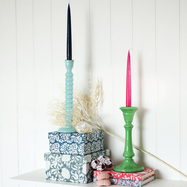 Seashell  Blue candle holder placed on a couple of hand painted boxes.Next to this is another candle holder placed on a couple of hand blocked painted notebooks.Both have contrasting candles in them,there are shells also in the picture