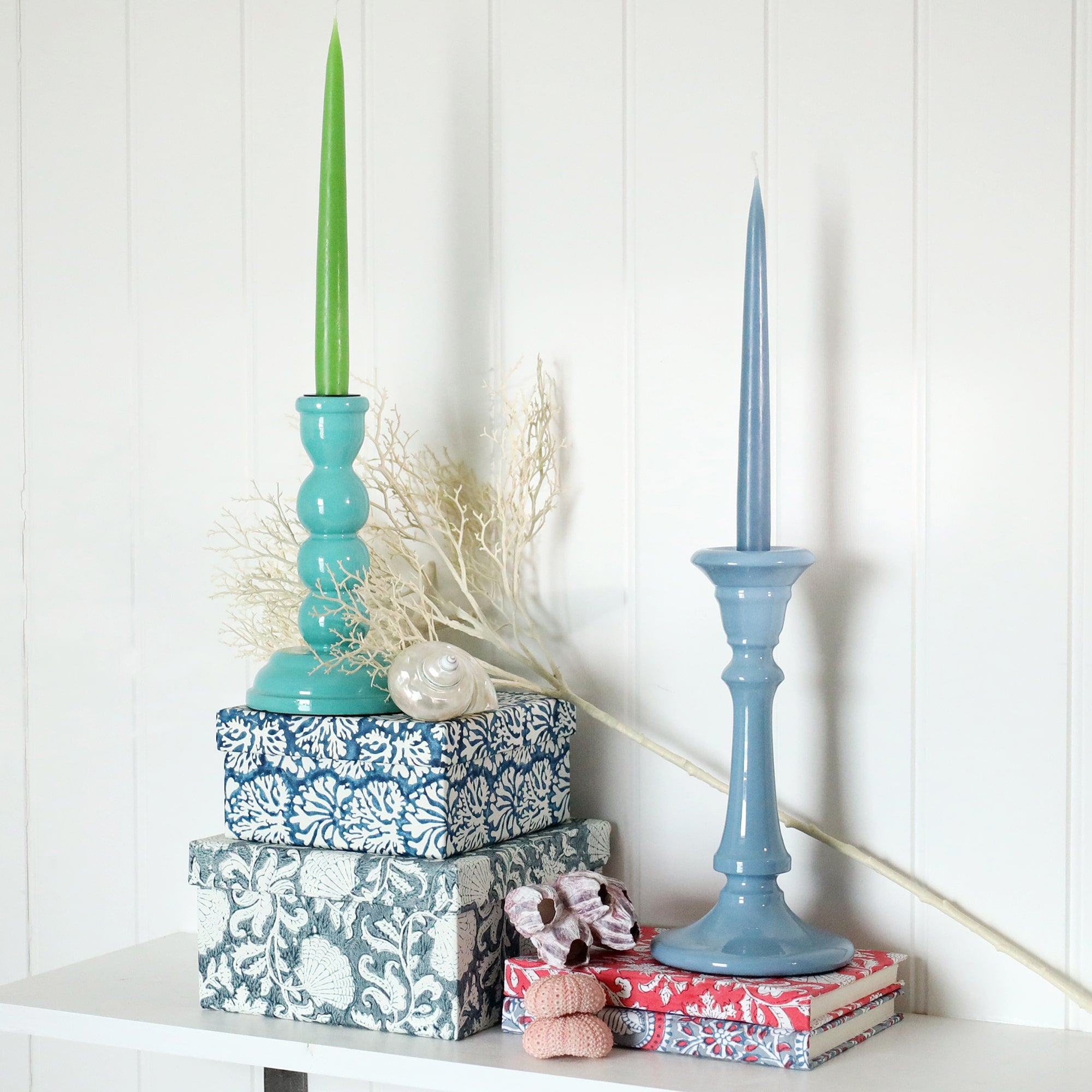 Turquoise candle holder placed on a couple of hand painted boxes.Next to this is Tidal candle holder placed on a couple of hand blocked painted notebooks.Both have matching candles in them,there are shells also in the picture